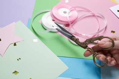 Photo of Woman cutting ribbon with beautiful scissors near colorful paper sheets, closeup