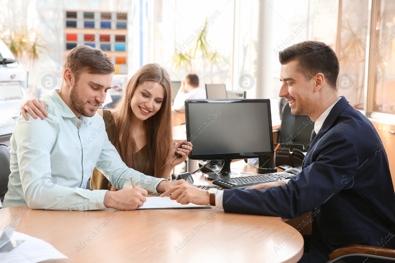 Photo of Young couple and salesman sitting at table in car salon. Buying auto