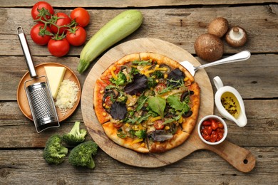 Delicious vegetarian pizza and ingredients on wooden table, flat lay