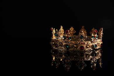 Photo of Beautiful golden crown with gems on dark mirror surface. Space for text