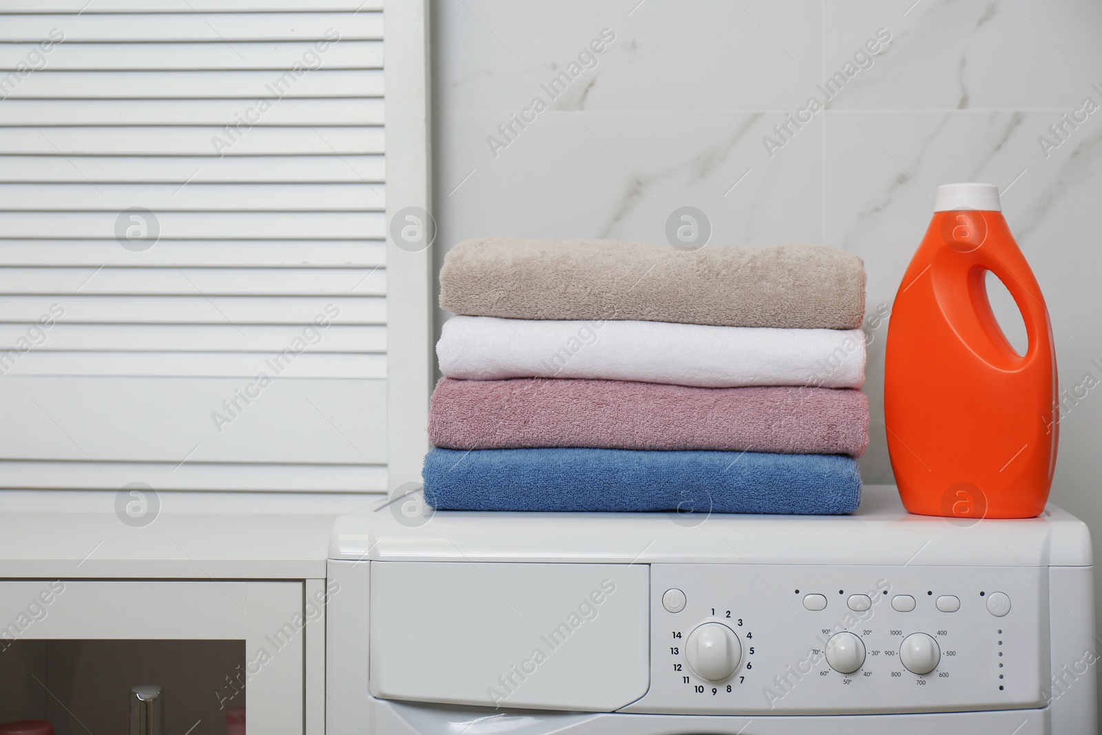 Photo of Stack of fresh towels and detergent on washing machine in laundry room