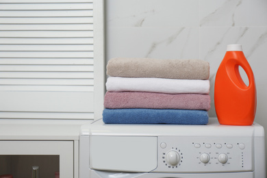Photo of Stack of fresh towels and detergent on washing machine in laundry room