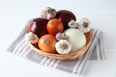 Photo of Fresh raw garlic and onions in wicker basket on white table