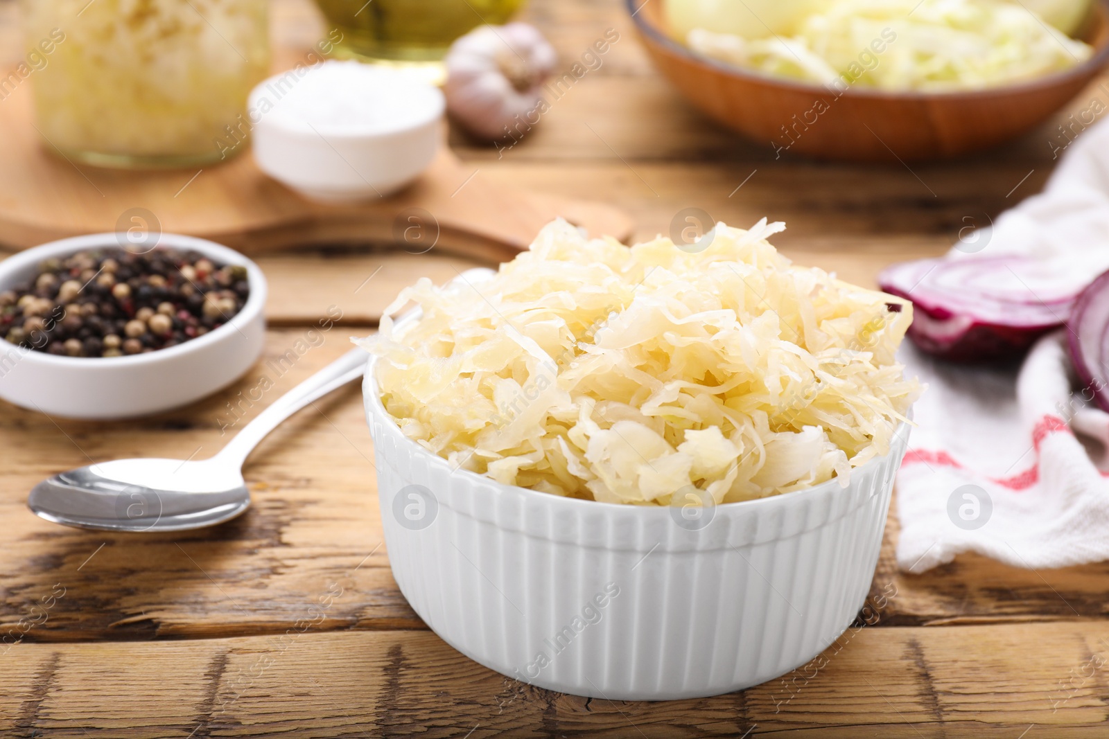 Photo of Bowl of tasty sauerkraut and ingredients on wooden table, closeup