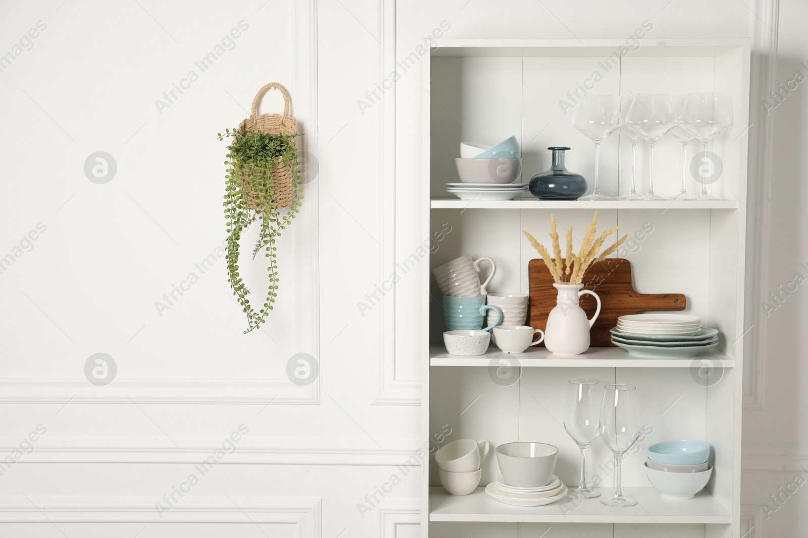 Photo of Different clean dishware and glasses on shelves in cabinet indoors