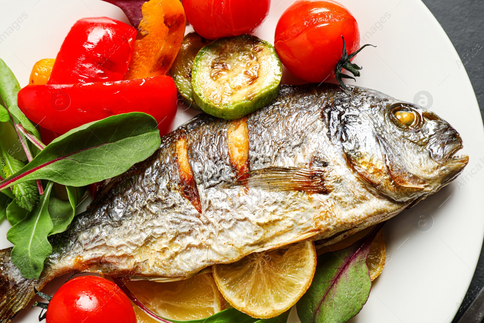 Photo of Delicious roasted fish with lemon and vegetables on plate, flat lay