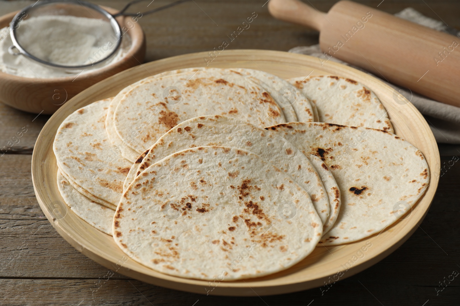 Photo of Many tasty homemade tortillas and rolling pin on wooden table