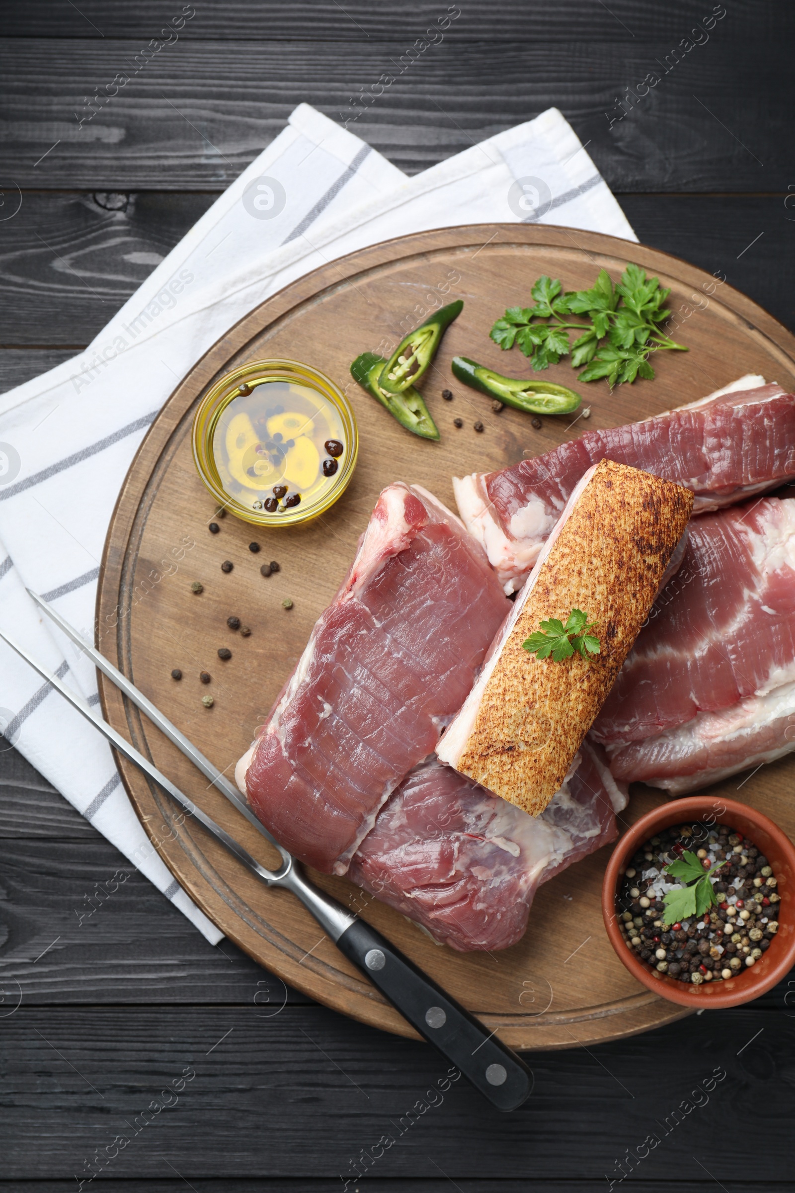 Photo of Pieces of raw pork belly, chili pepper, peppercorns, oil and parsley on black wooden table, top view