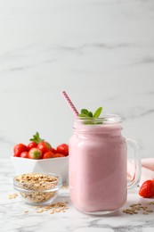 Mason jar of tasty strawberry smoothie with oatmeal and mint on white marble table, space for text