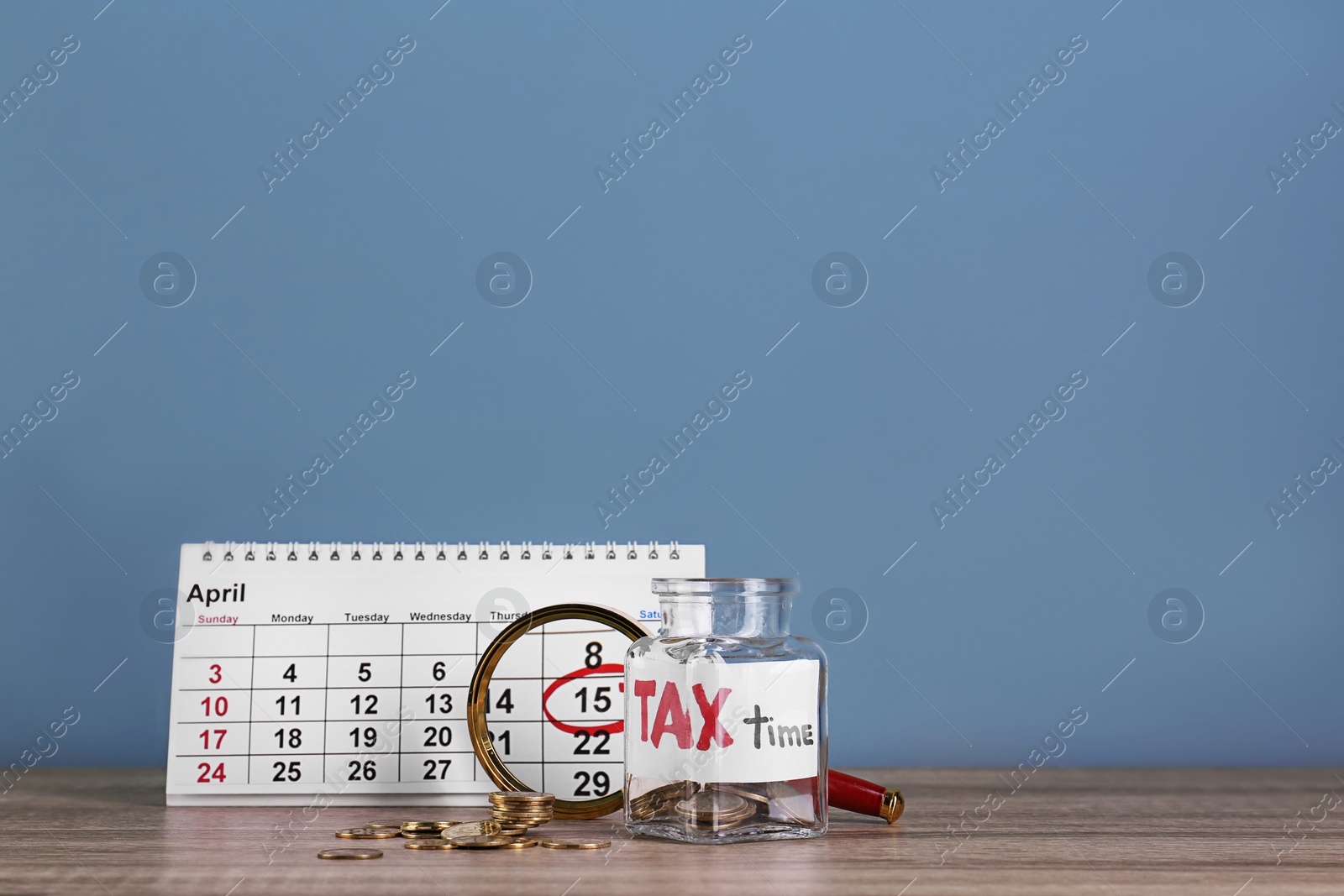 Photo of Calendar, glass jar with label "TAX TIME" and coins on table