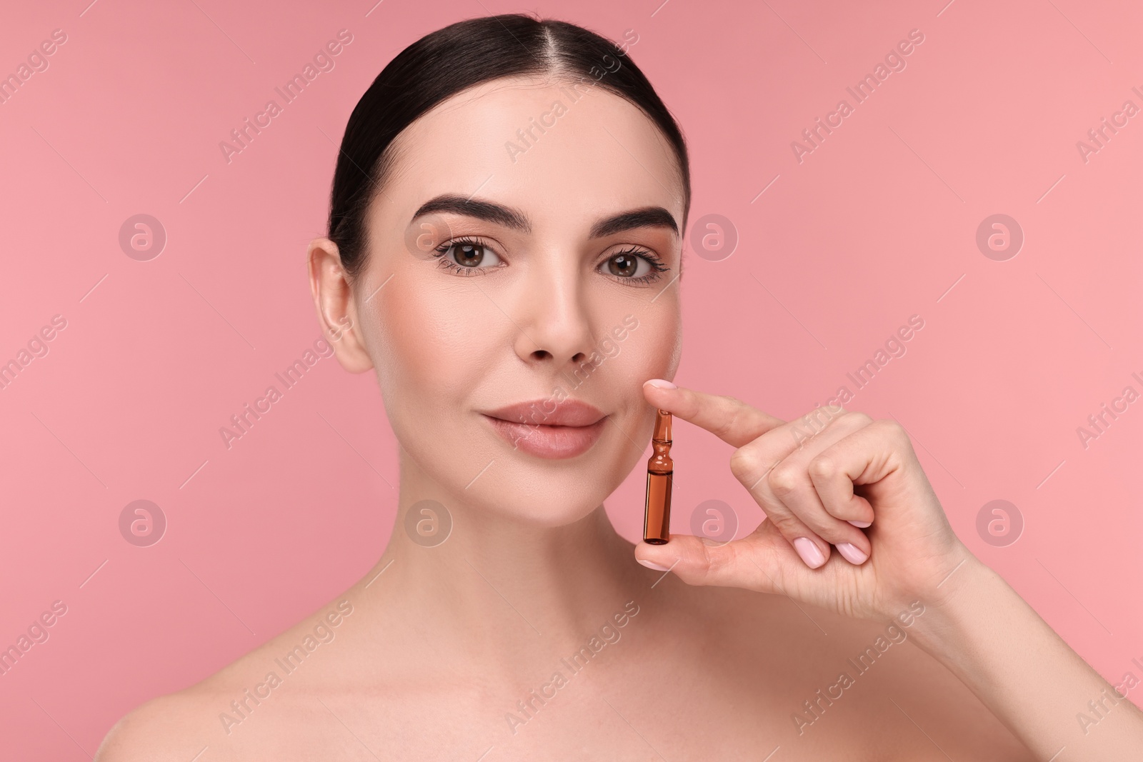 Photo of Beautiful young woman holding skincare ampoule on pink background