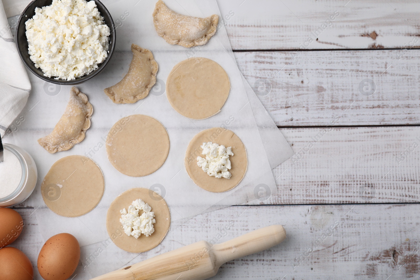 Photo of Process of making dumplings (varenyky) with cottage cheese. Raw dough and ingredients on white wooden table, flat lay. Space for text