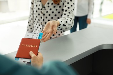 Photo of Agent giving passport and ticket to woman at check-in desk in airport, closeup