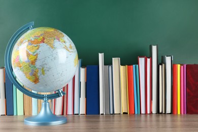 Photo of Globe and many books on wooden table near green chalkboard. Geography lesson