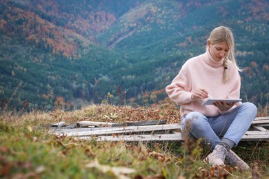 Young woman drawing on tablet in mountains, space for text