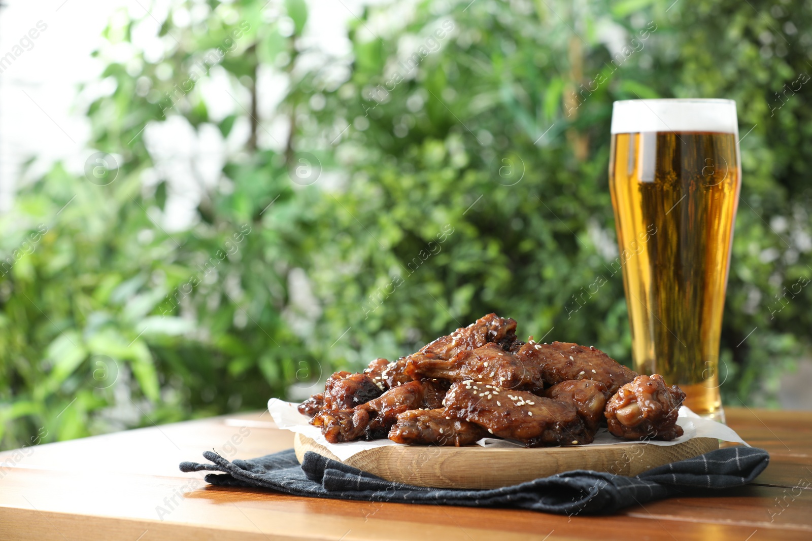 Photo of Tasty roasted chicken wings served with beer on wooden table. Space for text