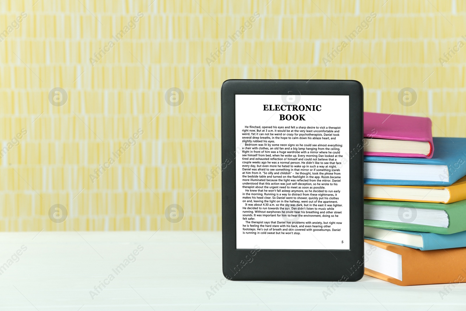 Image of Portable e-book reader and stack of books on white wooden table, space for text