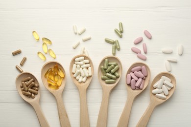 Photo of Different vitamin capsules in spoons on white wooden table, flat lay