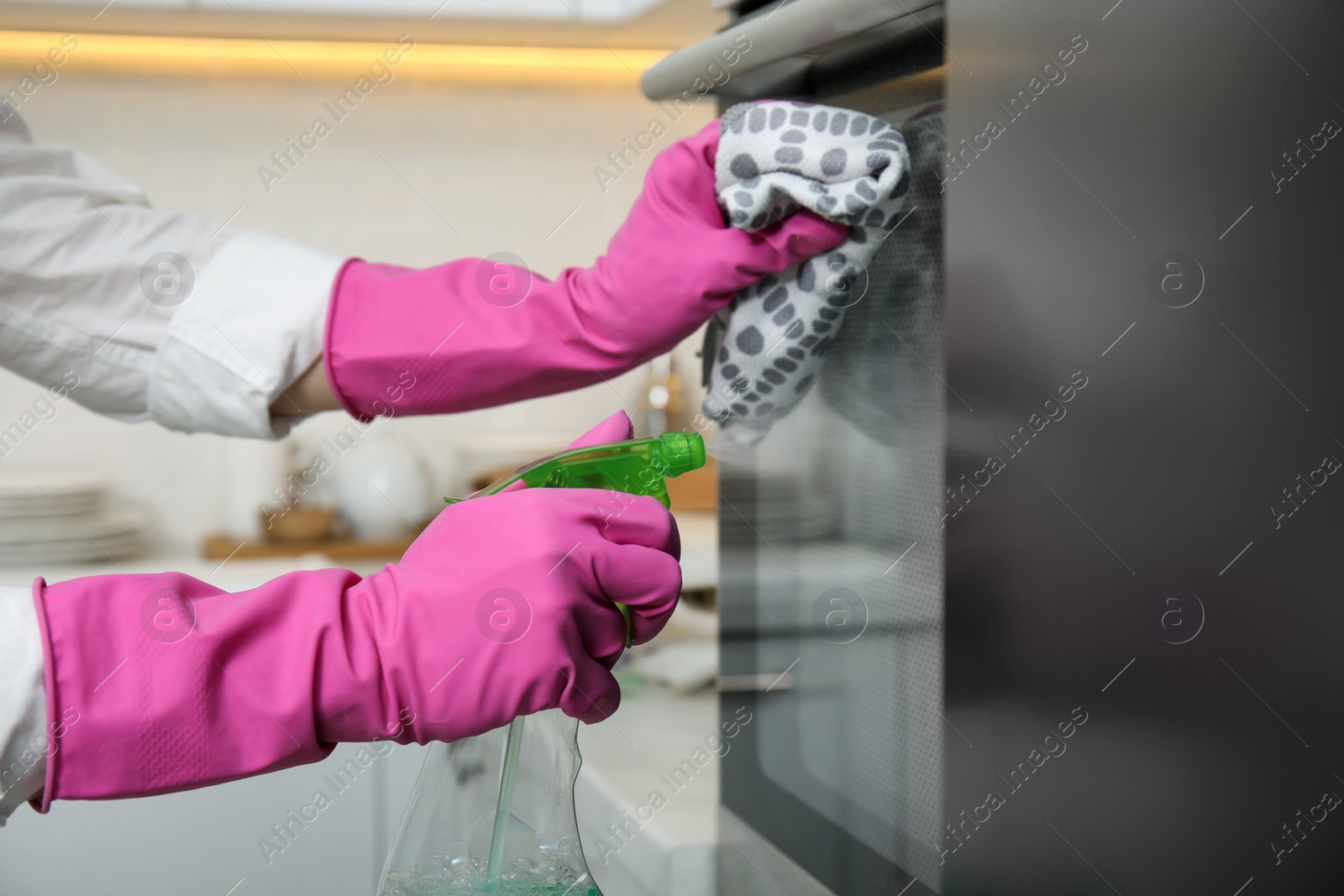 Photo of Woman cleaning oven with rag and detergent in kitchen, closeup