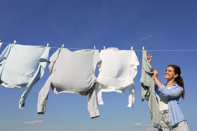 Photo of Woman hanging clothes with clothespins on washing line for drying against blue sky