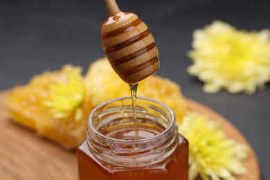 Photo of Pouring sweet honey from dipper into jar at table, closeup