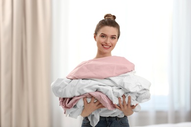 Woman holding pile of dirty laundry indoors