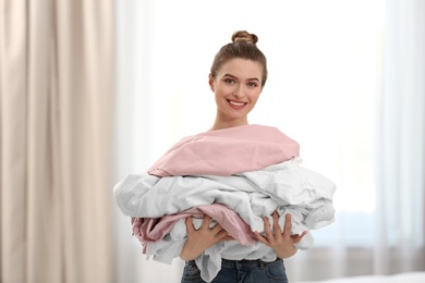 Photo of Woman holding pile of dirty laundry indoors