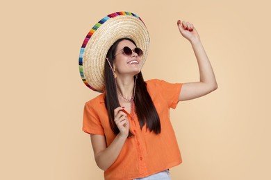 Photo of Young woman in Mexican sombrero hat and sunglasses dancing on beige background