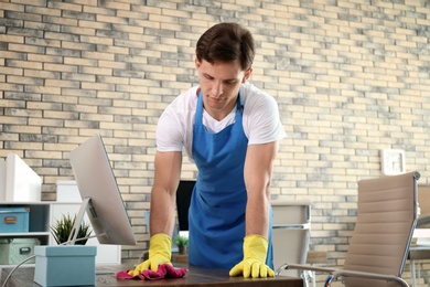 Young man in apron and gloves cleaning office