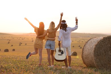 Photo of Hippie friends with guitar showing peace signs in field, back view