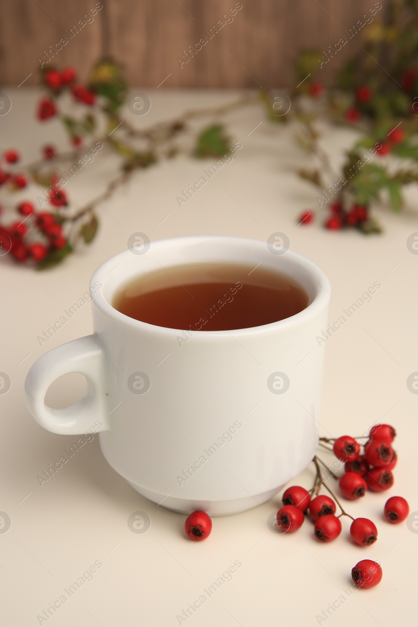 Photo of Aromatic hawthorn tea in cup and berries on beige table, closeup