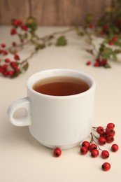 Aromatic hawthorn tea in cup and berries on beige table, closeup