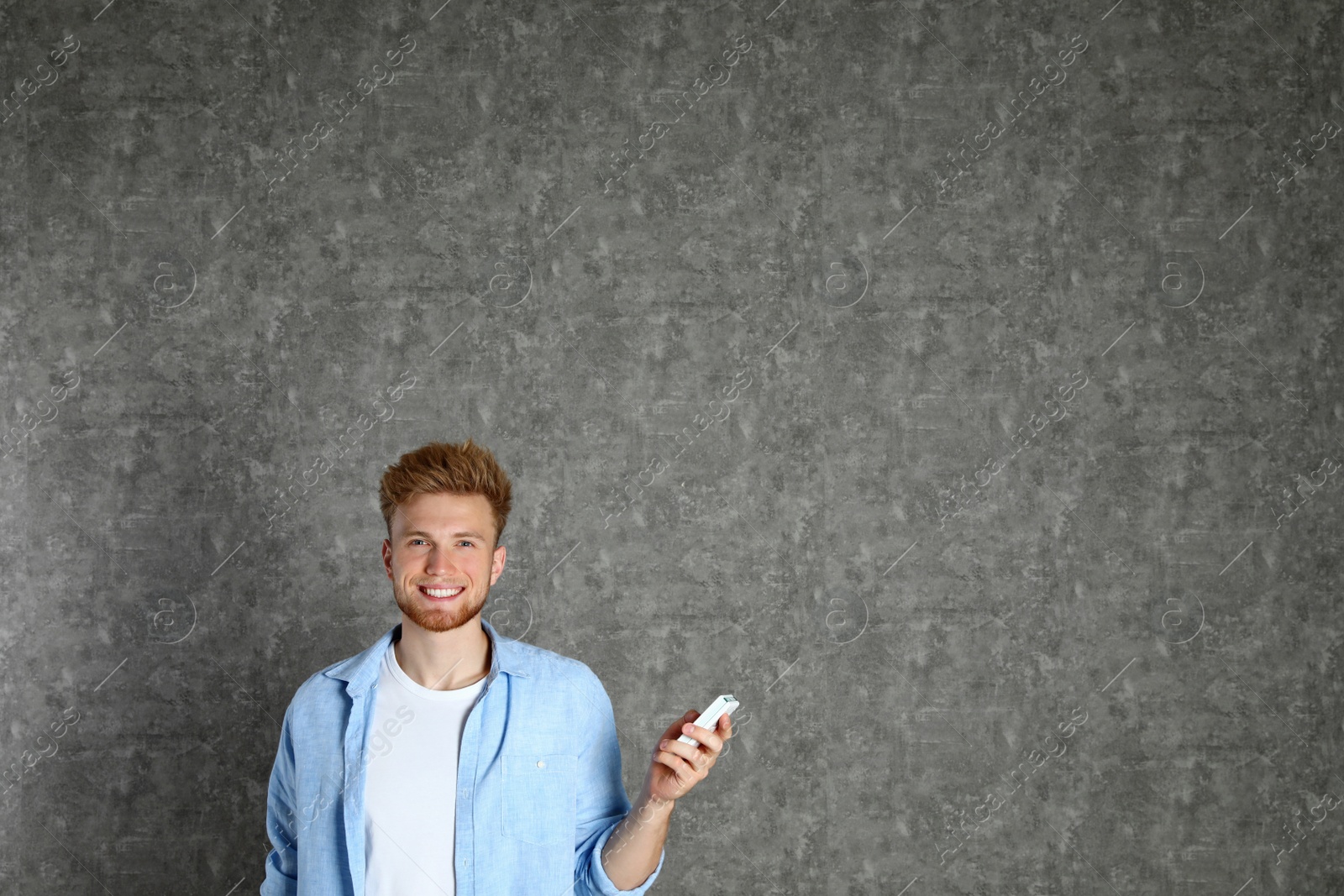 Photo of Young man with air conditioner remote on grey background. Space for text