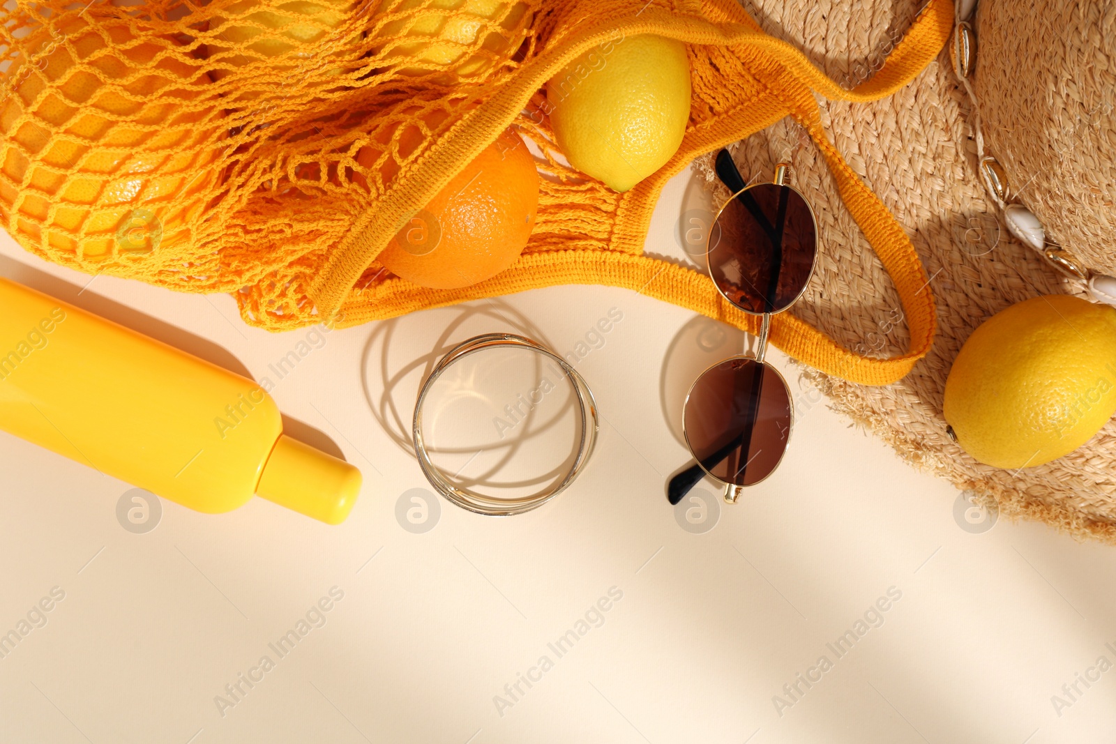 Photo of String bag with sunglasses, fruits and summer accessories on beige background, flat lay. Space for text