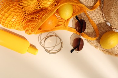 String bag with sunglasses, fruits and summer accessories on beige background, flat lay. Space for text