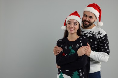 Happy young couple in Christmas sweaters and Santa hats on grey background. Space for text