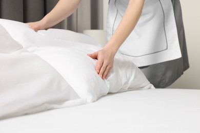 Photo of Young maid making bed in hotel room, closeup