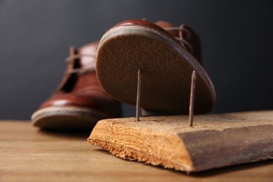 Photo of Metal nails in wooden plank and shoes on table, closeup