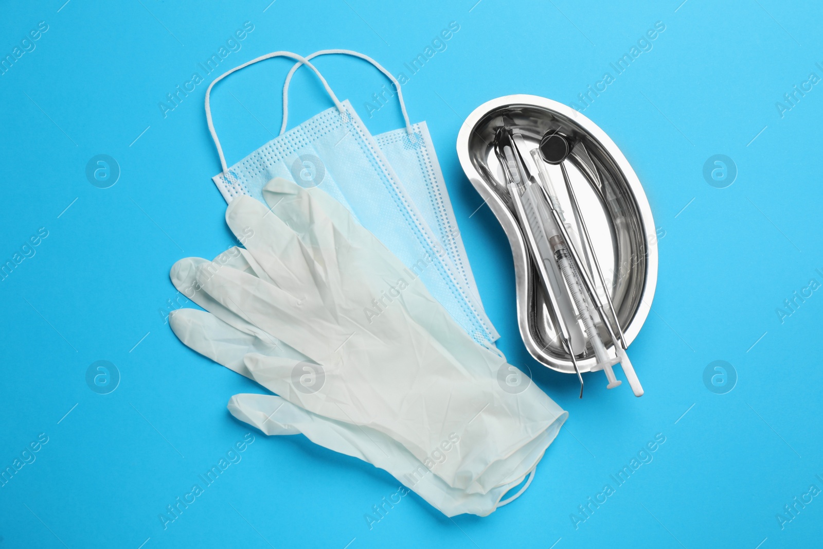 Photo of Set of different dentist's tools, face masks and gloves on light blue background, flat lay