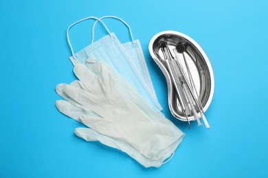 Photo of Set of different dentist's tools, face masks and gloves on light blue background, flat lay