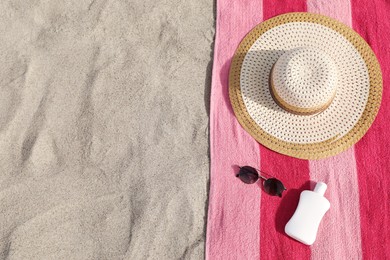 Beach towel with straw hat, sunglasses and sunscreen on sand, flat lay. Space for text