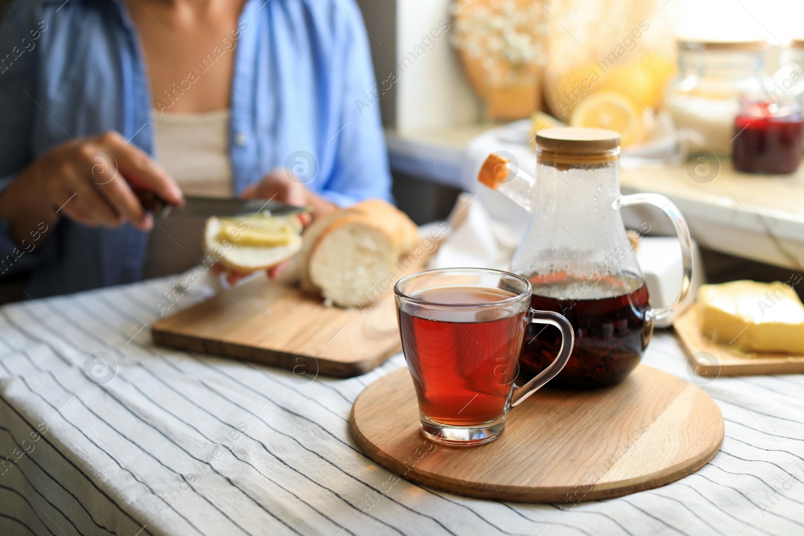 Photo of Woman spreading butter onto bread at table indoors, focus on aromatic tea