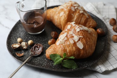 Delicious croissants with chocolate, nuts and spoon on white marble table, closeup