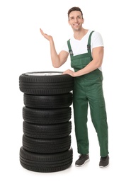 Photo of Young mechanic in uniform with car tires on white background