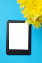 Photo of E-book reader with flowers on light blue background, top view. Space for text