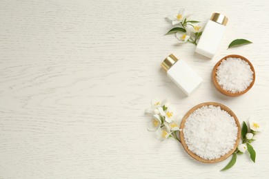 Beautiful jasmine flowers, skin care products and sea salt on white wooden table, flat lay. Space for text