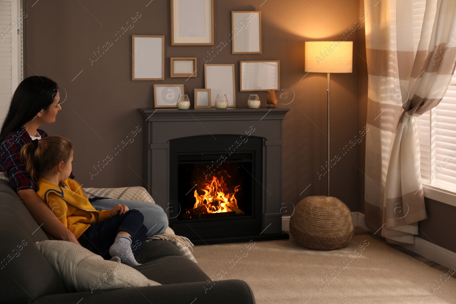 Photo of Happy mother and daughter spending time together on sofa near fireplace at home. Space for text