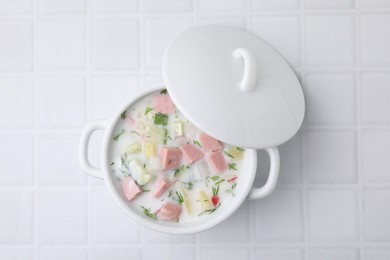 Photo of Delicious cold summer soup (okroshka) with boiled sausage in pot on white tiled table, top view