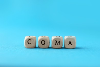 Wooden cubes with word Coma on light blue background, closeup