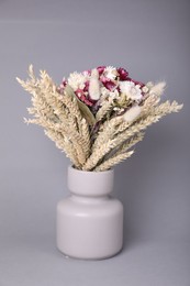 Bouquet of beautiful dry flowers and spikelets in vase on grey background